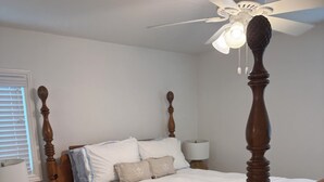 Quarto com cama de dossel, ventoinha no teto, mesa de cabeceira com abajur e criado-mudo com luminária.