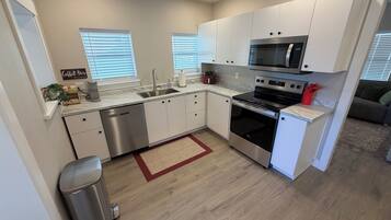 A compact kitchen with white cabinets, a stainless steel dishwasher, a microwave, and an oven.