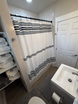 A bathroom with a white sink, a toilet, a towel rack with folded towels, and a striped shower curtain. - Charming 3BR/1BA Burley home w/ full yard, near park, shops & Snake River (Burley)