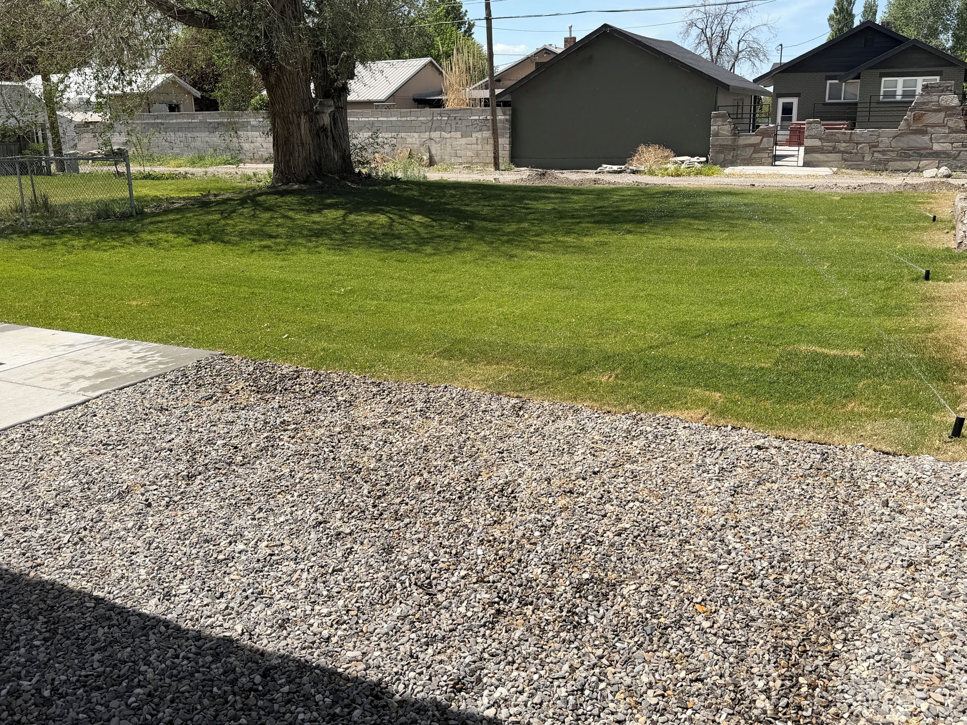 A residential area with a well-maintained lawn, a stone wall, and a house with a dark roof.