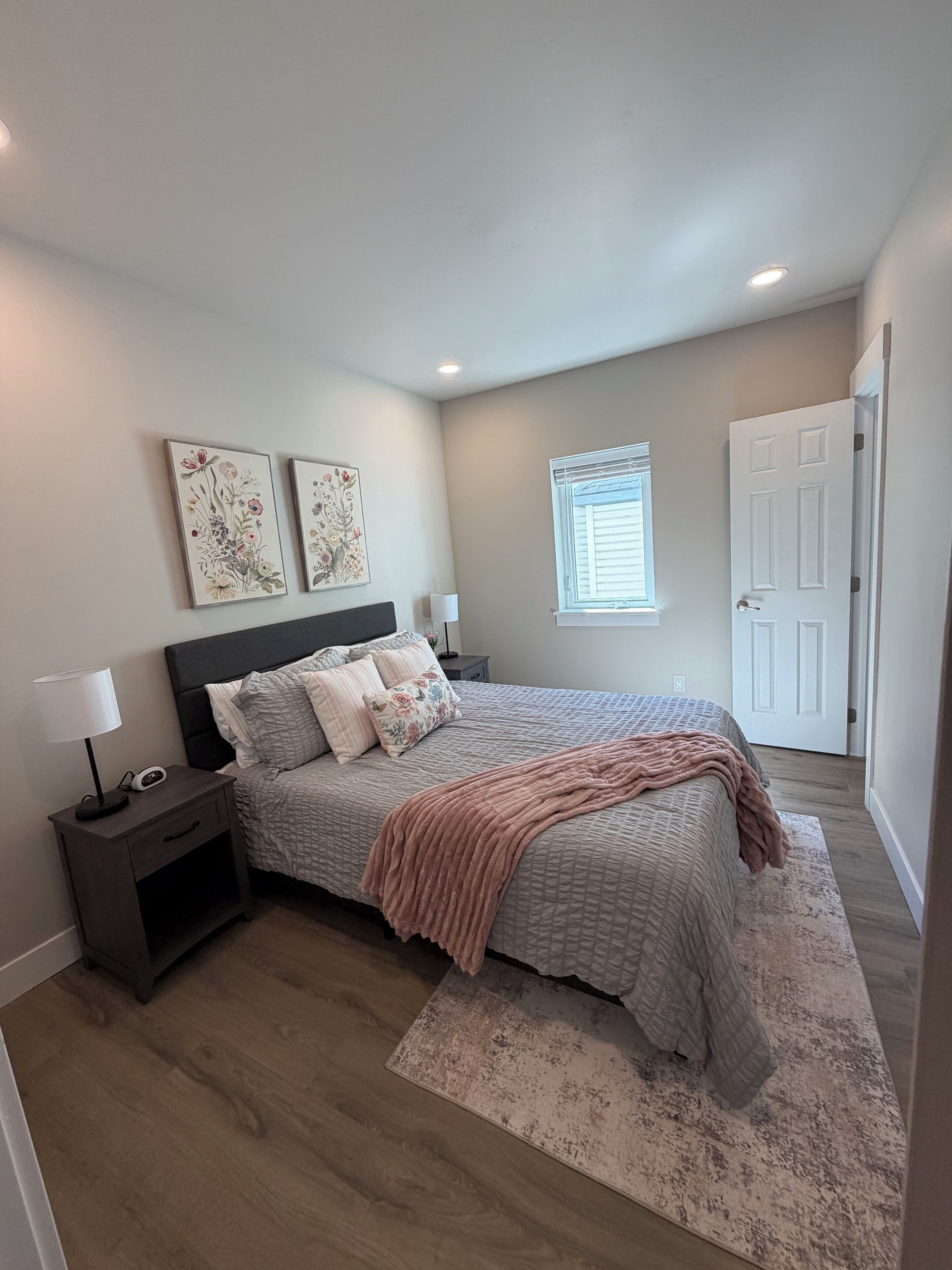 A bedroom with a bed, nightstands, a lamp, a window, and a door.