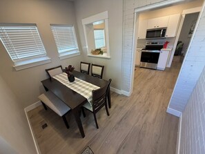 A dining area with a table and chairs, a kitchen in the background, and a window with blinds. - Charming 3BR/1BA Burley home w/ full yard, near park, shops & Snake River (Burley)