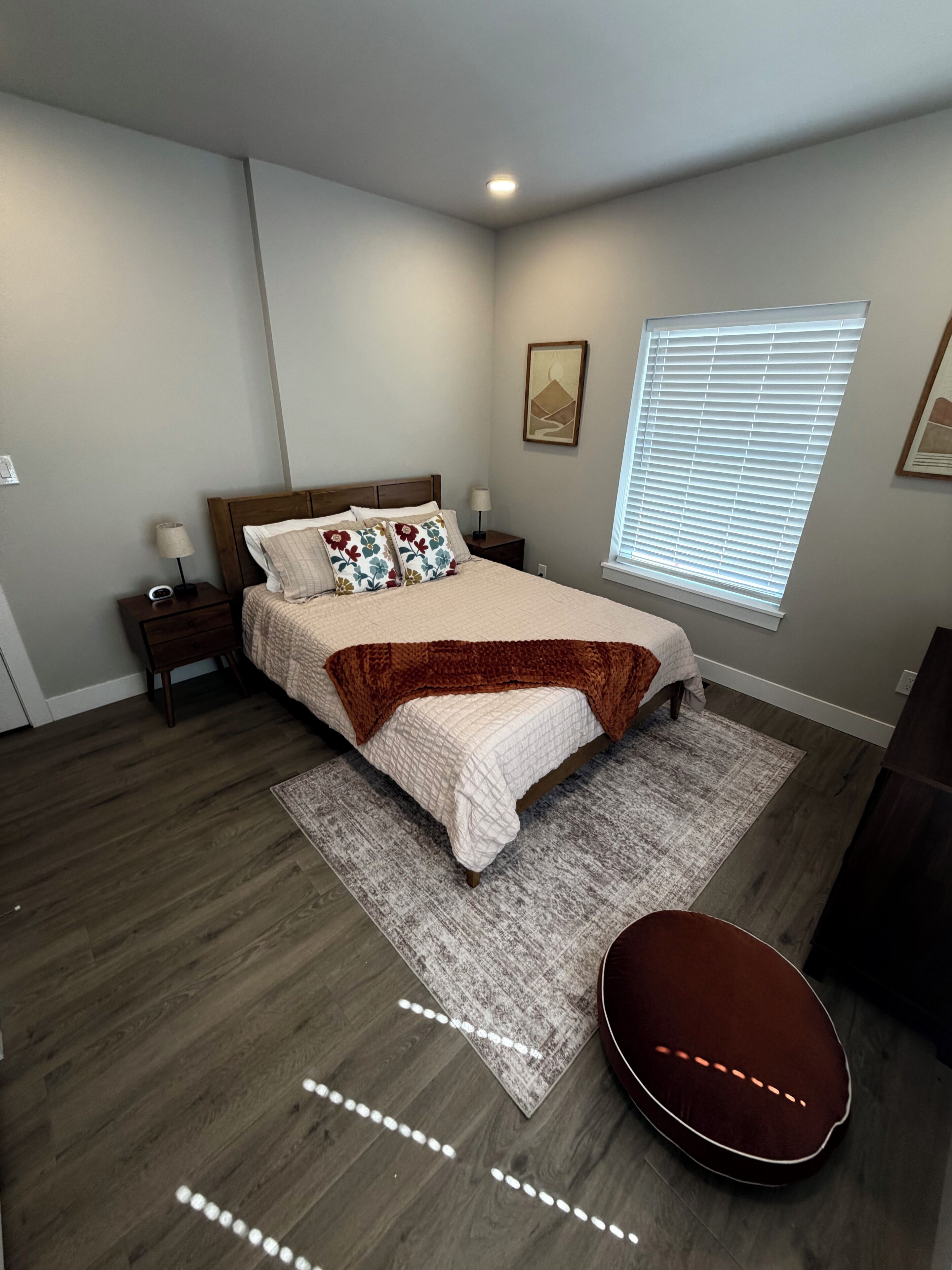 A bedroom with a bed, nightstands, a window with blinds, a rug, and a guitar.