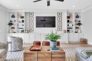 A modern living room with a flat-screen TV, wooden coffee table, patterned sofas, and white cabinetry with decorative items. - Luxury Massive Townhome, Pool, Private Elevator, Amenities in Murfreesboro (Murfreesboro)