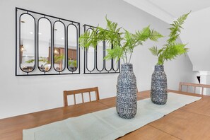 Een eetgedeelte met een houten tafel, twee decoratieve vazen met groene planten, en een modern kunstwerk op de muur.