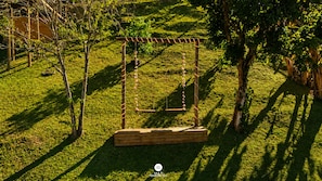 A wooden swing set in a grassy area with trees and a wooden structure in the background.