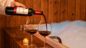 Une main verse du vin dans deux verres sur un comptoir en bois, avec une bougie et un seau à glace en arrière-plan.