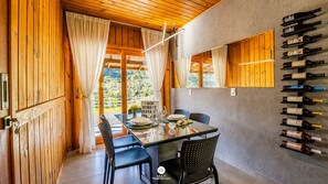 Een eetruimte met een glazen tafel, stoelen en een wijnrek met flessen.