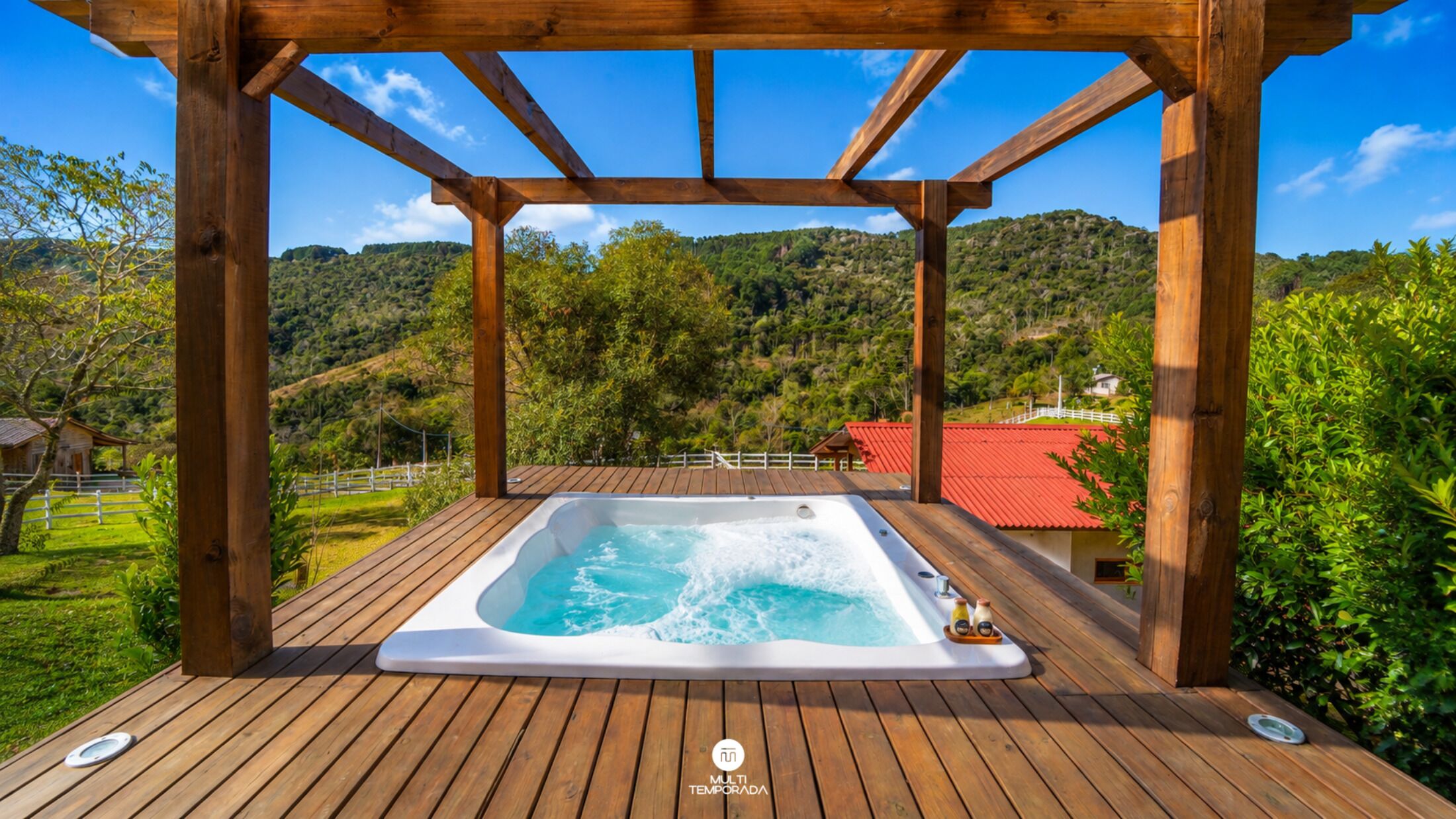 A wooden deck with a hot tub surrounded by a pergola, overlooking a mountainous landscape.