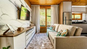 Una sala de estar acogedora con un sofá, un televisor montado en una pared de mármol, techo de madera y vistas al exterior a través de una ventana.