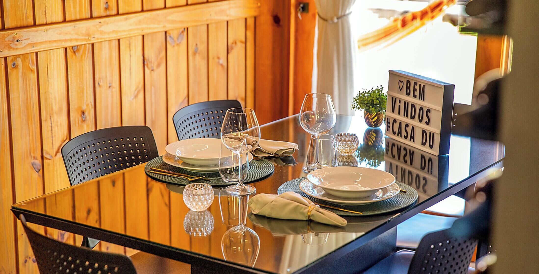A dining table set with plates, glasses, and cutlery, with a signboard in the background.
