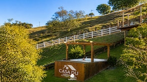 A wooden structure with a sign reading 'CASADU ALFREDO WILMER MULTI TEMPORADA' on a grassy hill with a white fence and trees in the background.