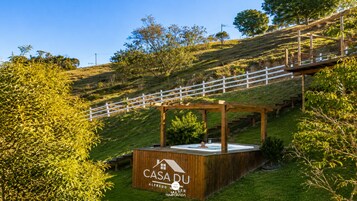 Estrutura de madeira com uma placa indicando 'CASADU ALFREDO WILMER MULTI TEMPORADA' em uma colina gramada com cerca branca e árvores ao fundo.