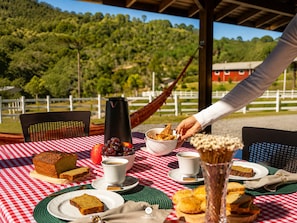 A table set with food and drinks, a hammock, and a view of a forested hill.