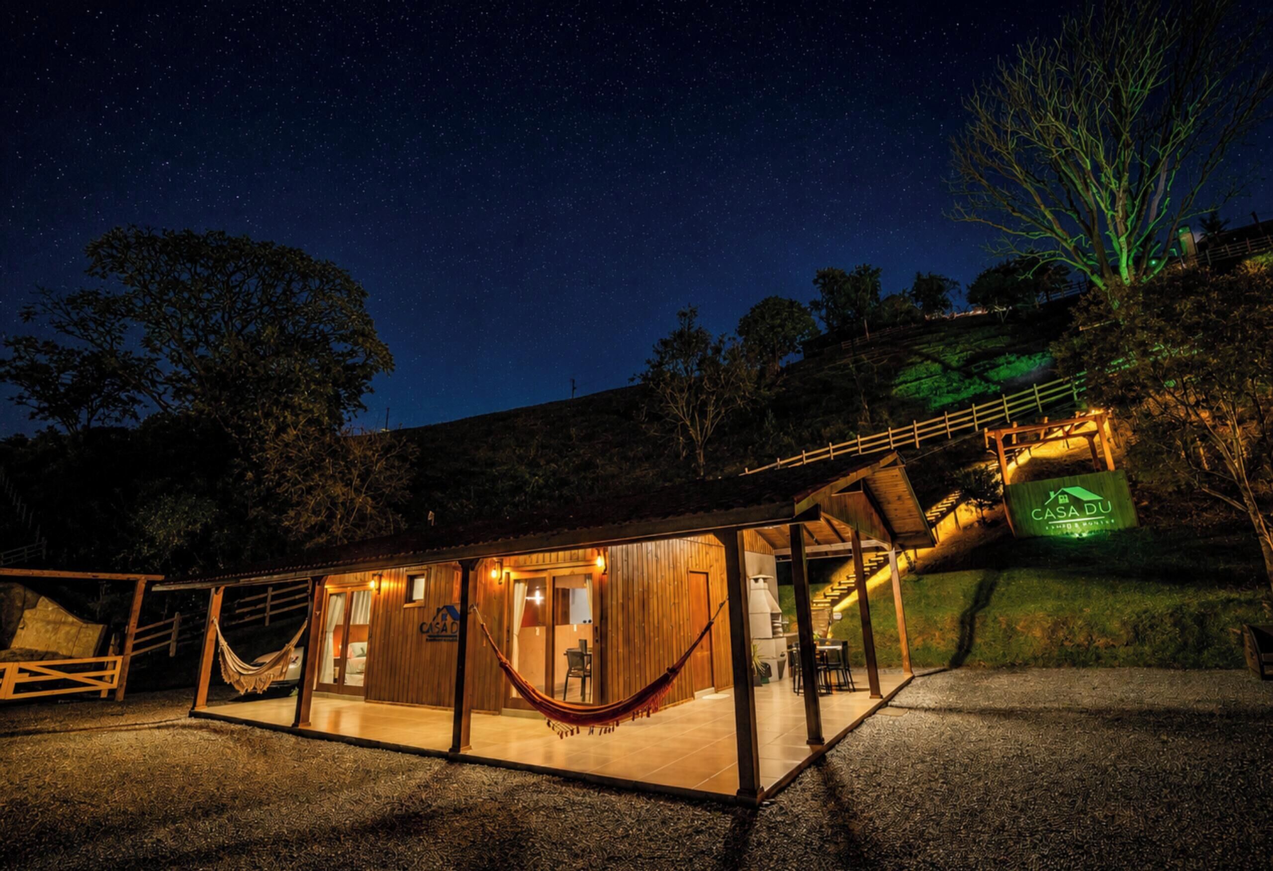 A wooden cabin with a hammock, a dining area, and a view of the night sky.