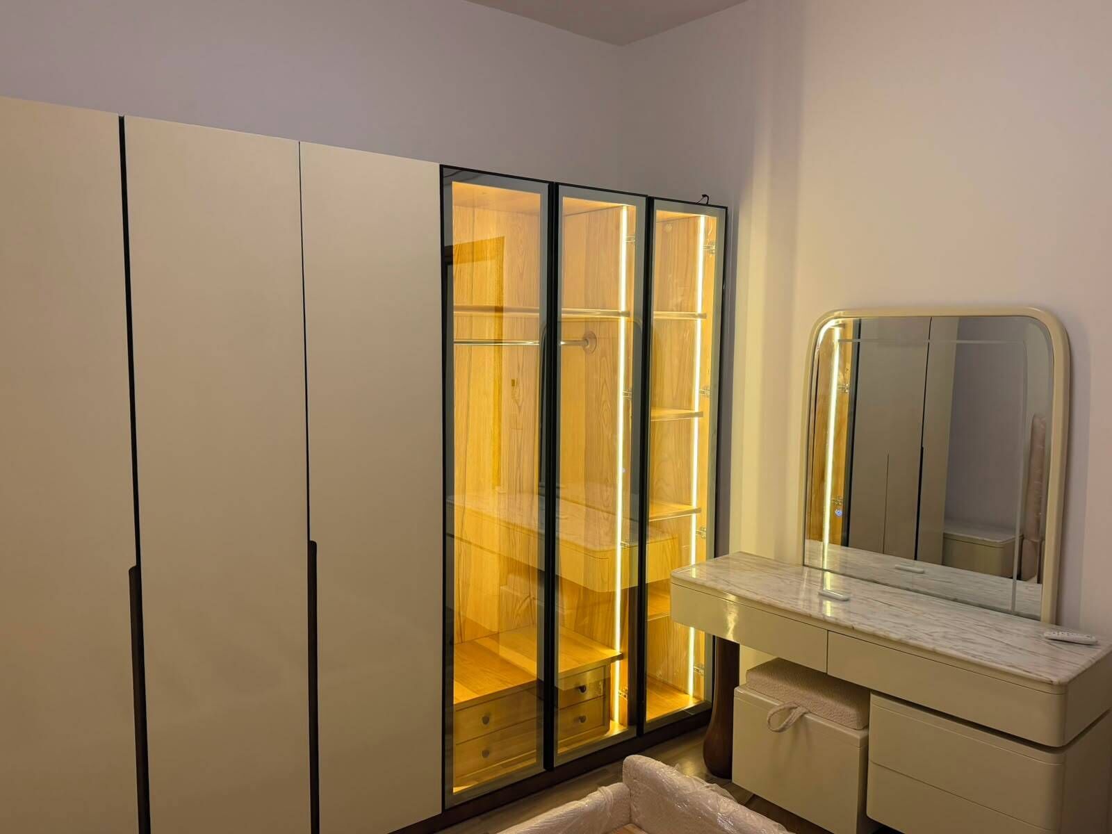 A bathroom with a vanity, mirror, and a wardrobe with glass doors.