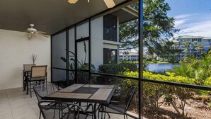 Varanda com mesa e cadeiras, vista para um corpo de água e vegetação.