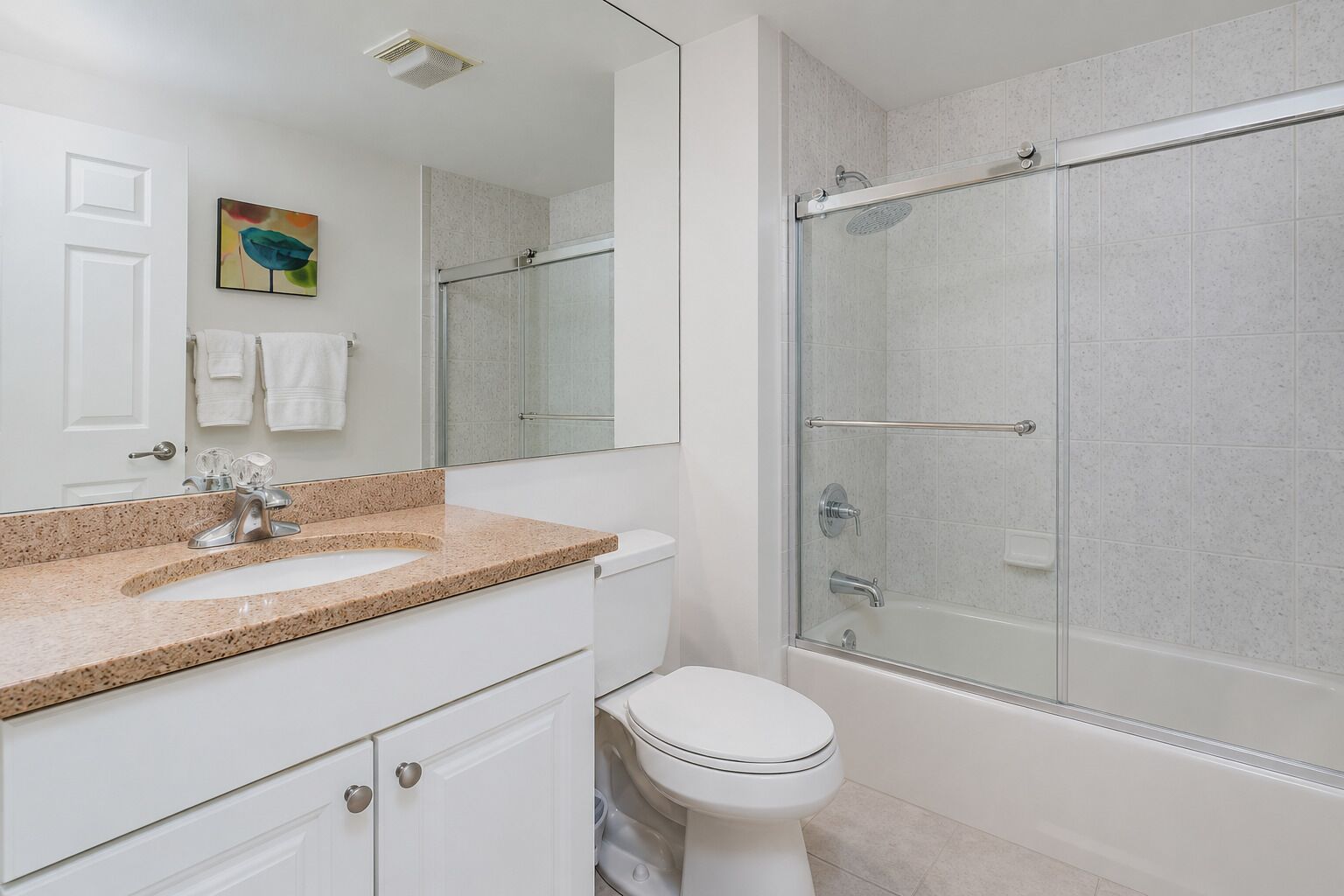 Un baño moderno con ducha de vidrio, inodoro blanco y lavamanos con encimera de granito.