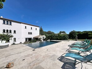 A pool area with lounge chairs and a white building with multiple windows.