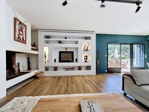Een moderne woonkamer met een open haard, een inbouwmeubel en een groot raam met uitzicht op de omgeving.