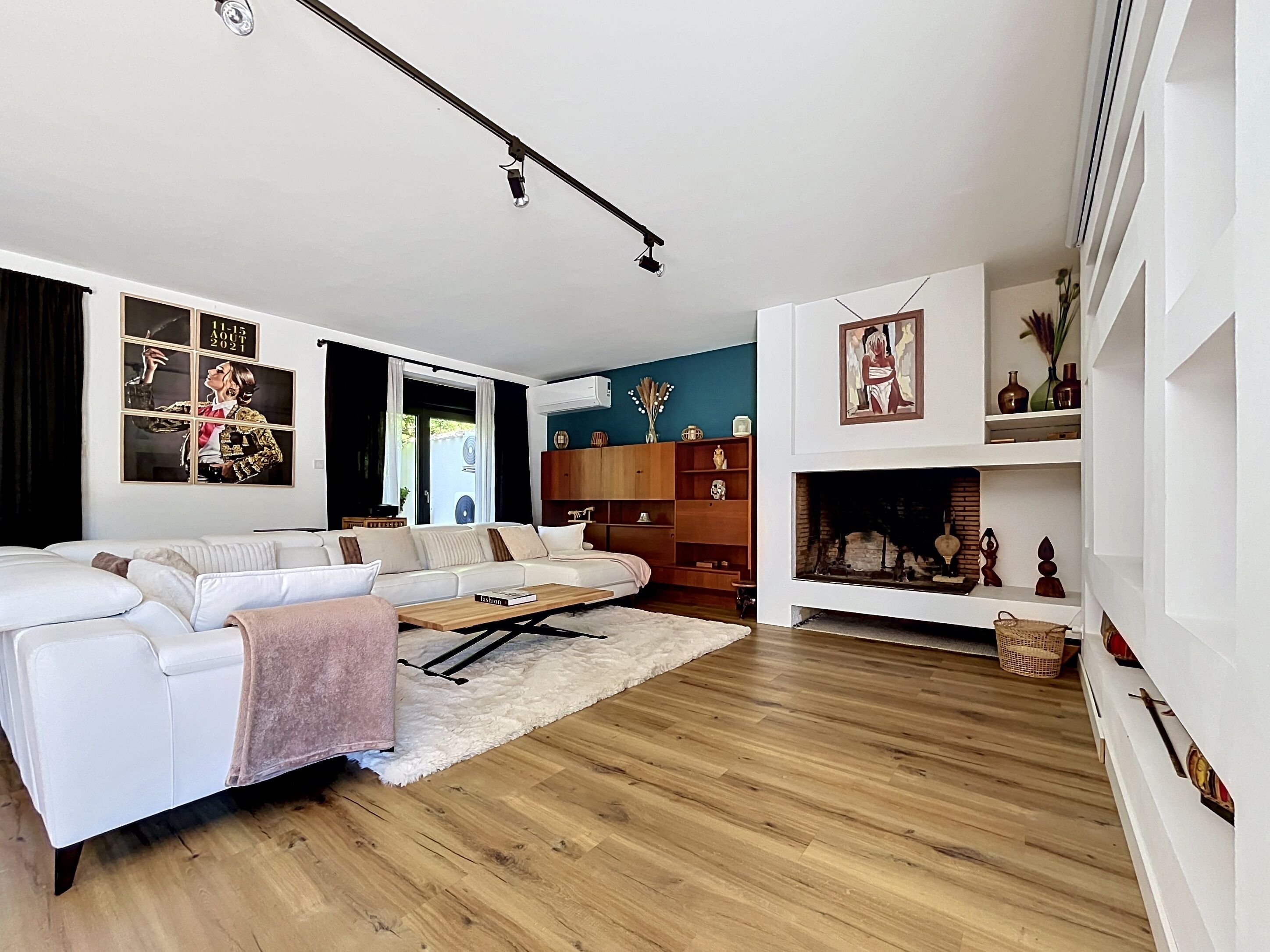 Un salon moderne avec un canapé blanc, un parquet en bois, une cheminée et une bibliothèque.