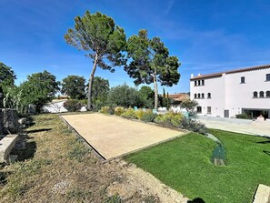 A courtyard with a tennis court, a grassy area, and a white building with arched windows.