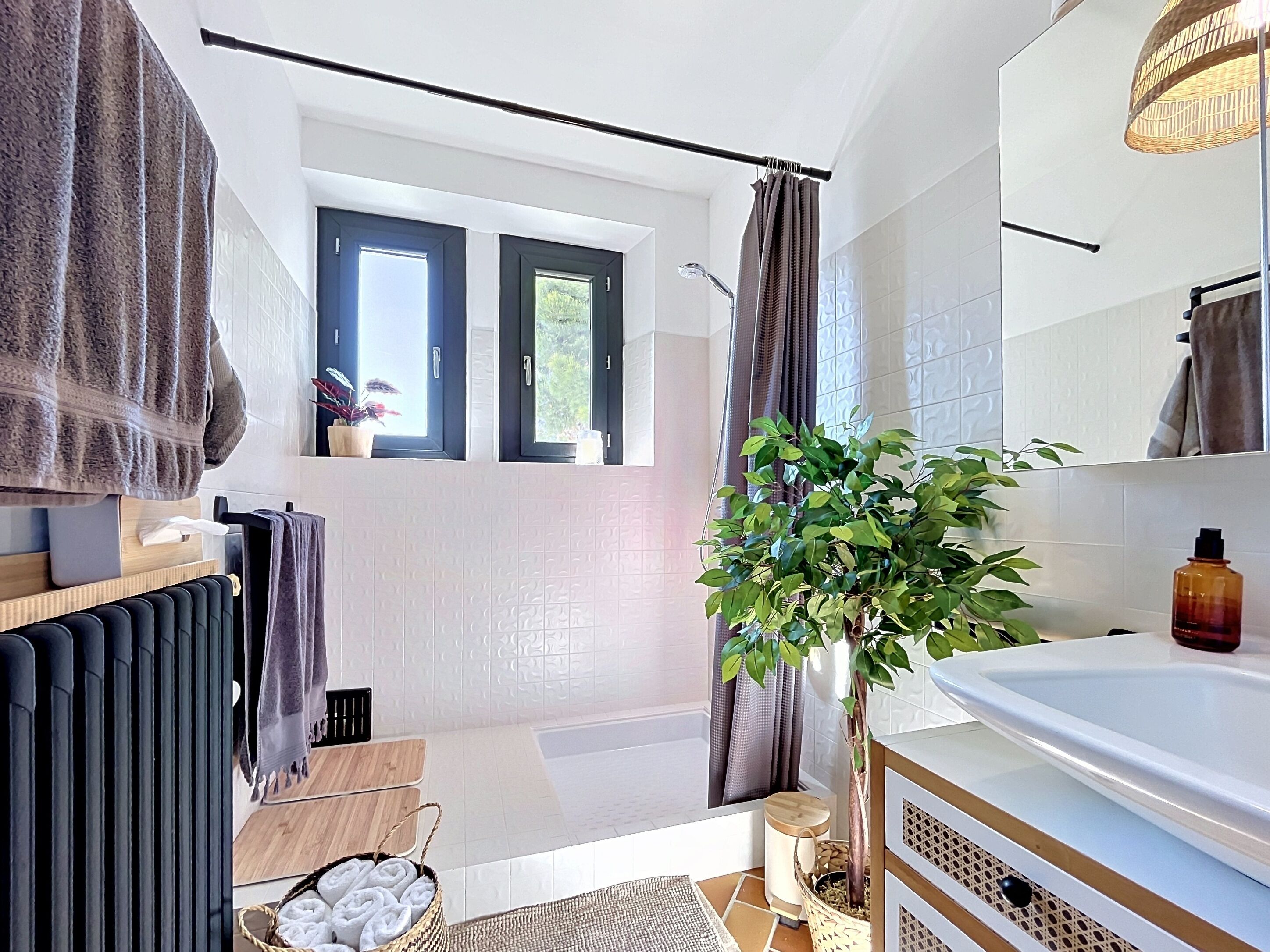 Une salle de bain moderne avec une baignoire, un grand miroir, une plante en pot et une fenêtre avec des rideaux.