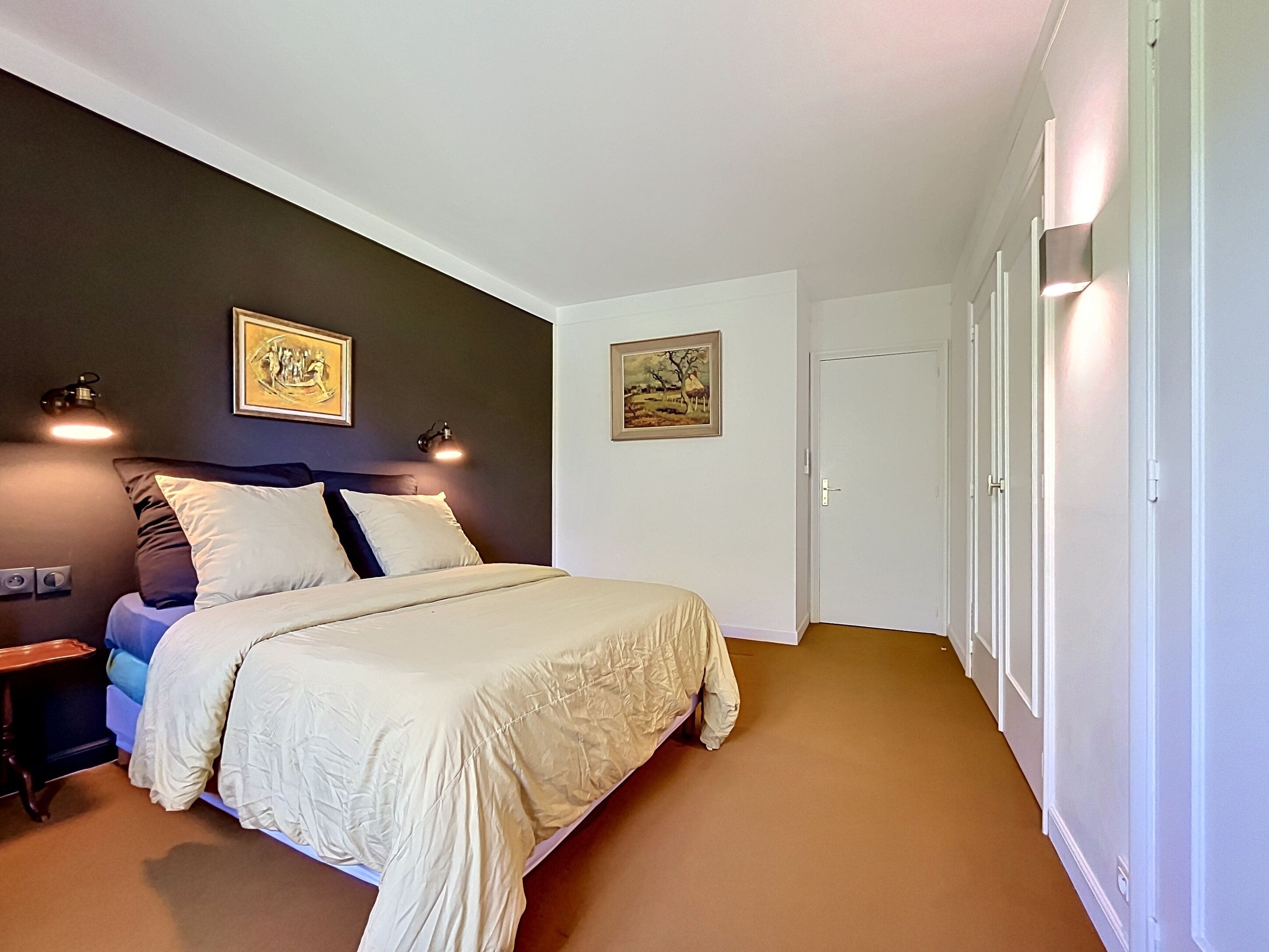 Ein Schlafzimmer mit einem Bett, zwei Wandlampen, einer Tür und zwei gerahmten Bildern.