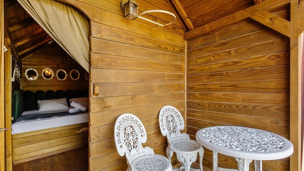A wooden cabin interior with a bed, two chairs, a table, and a hanging light fixture. - Magic Cabin Near Beto Carrero Trs0002 (Penha)