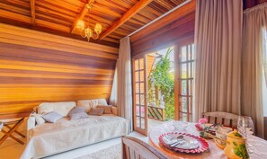 A cozy room with a wooden ceiling, a bed with patterned bedding, a dining table set with plates, glasses, and a teapot. - Magic Cabin in Front of Beto Carrero - Trs0003 (Penha)
