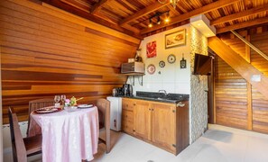 A cozy kitchen with wooden walls, a dining table set for two, and a staircase leading to an upper level. - Magic Cabin in Front of Beto Carrero - Trs0003 (Penha)