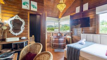A wooden cabin interior with a bed, wicker chairs, a wooden bathtub, and a television.