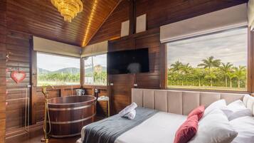 A wooden room with a bed, a TV, a large window, and a bathtub.