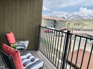 En balkon med udsigt til bjerge, en rød bil og en bygning med rødt tag.