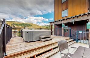 Une terrasse en bois avec un jacuzzi, une chaise et une vue sur un paysage vallonné.