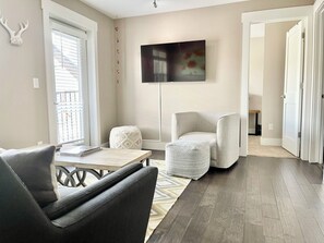 Ein modernes Wohnzimmer mit einer Couch, einem Sessel, einem Hocker und einem flachbildfernseher an der Wand.