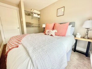Ein Hotelzimmer mit Bett, Nachttisch, Lampe, Ablage mit gefalteten Handtüchern und einer Tür.