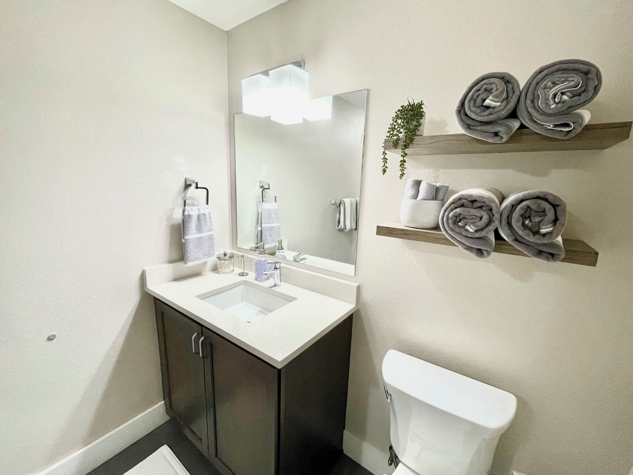 Une salle de bain avec un lavabo blanc, des meubles sombres, des toilettes et un espace de rangement pour les serviettes fixé au mur.