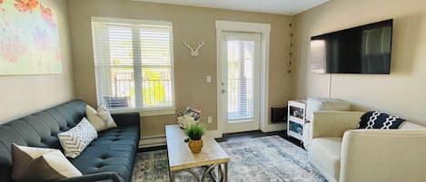 Una sala de estar con sofá, sillón, mesa de centro y televisor.