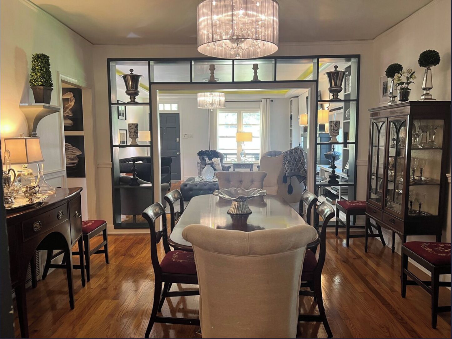 A dining area with a chandelier, wooden floor, and a view into another room.