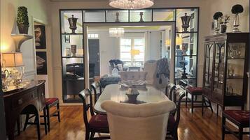 A dining area with a chandelier, wooden floor, and a view into another room.