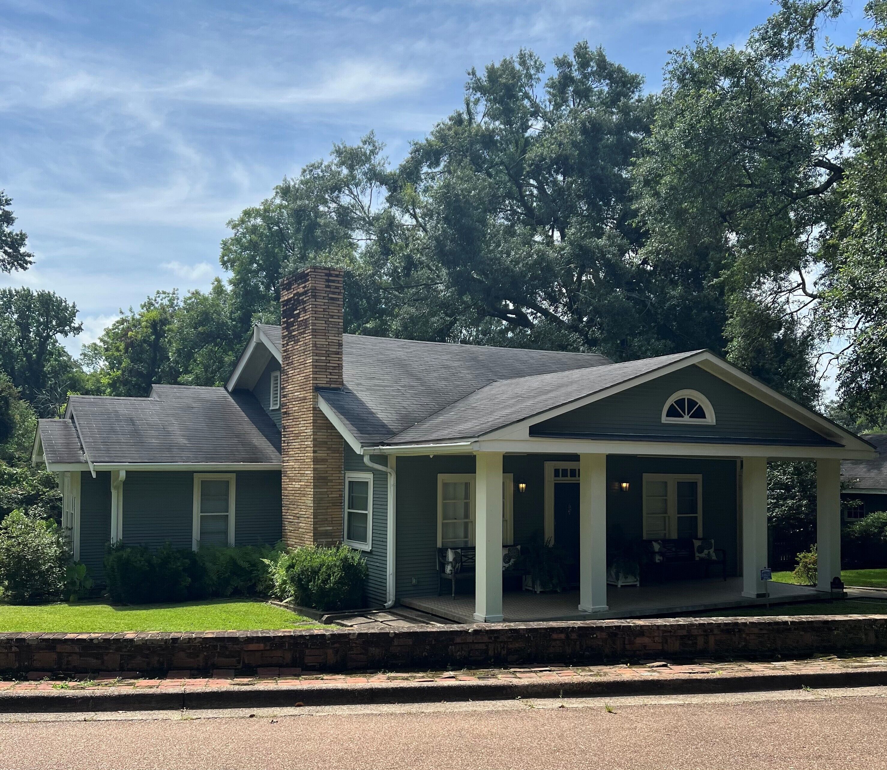 A two-story house with a brick chimney, a porch with white columns, and a green lawn.