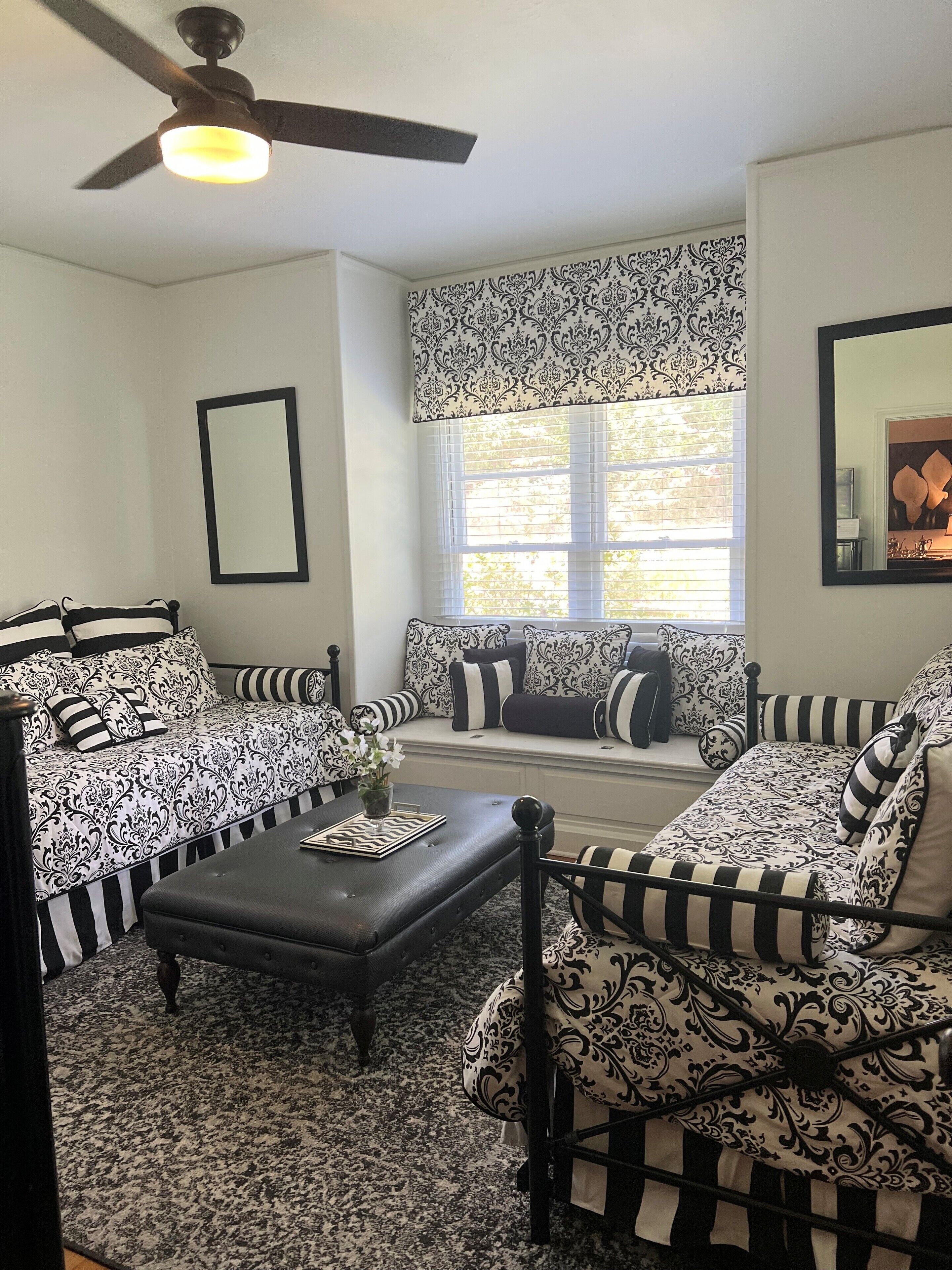A living room with a ceiling fan, patterned sofas, a coffee table, and a window with blinds.