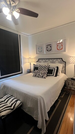 Un dormitorio con una cama, dos mesitas de noche, un ventilador de techo y decoración en la pared.