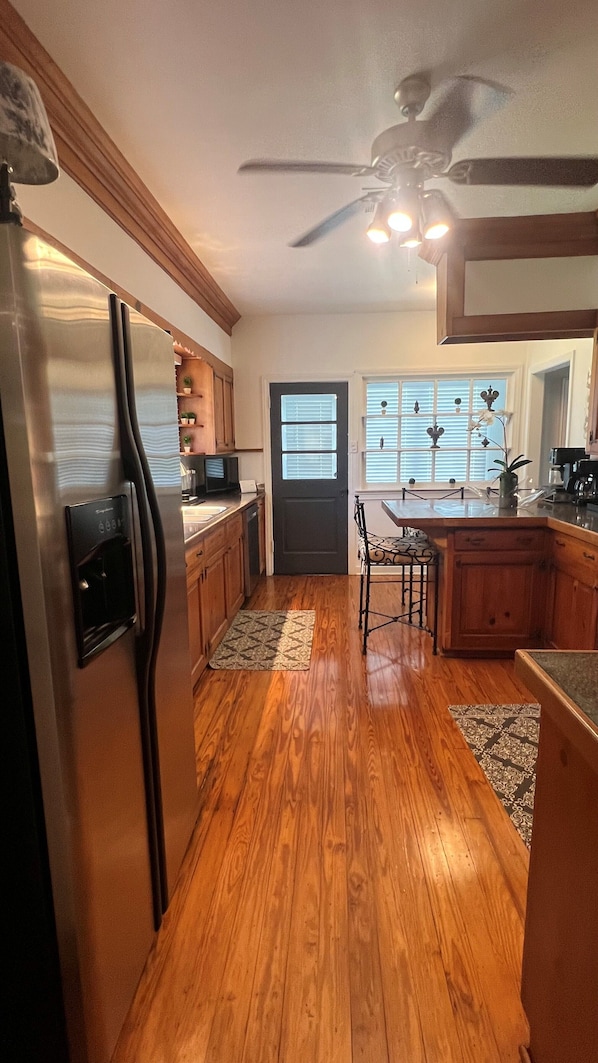 A kitchen with wooden cabinets, a refrigerator, a ceiling fan, and a dining area with a table and chairs.