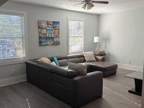 A modern living room with a sectional sofa, a glass coffee table, and a ceiling fan.