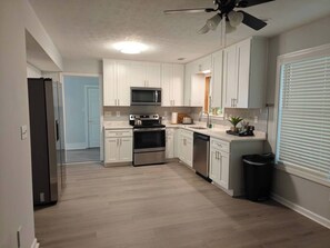 A modern kitchen with white cabinets, stainless steel appliances, and a ceiling fan.