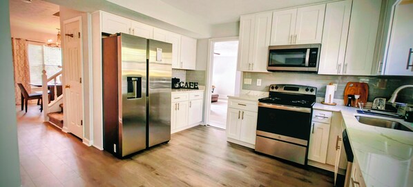 A modern kitchen with stainless steel appliances, white cabinetry, and a wooden floor.