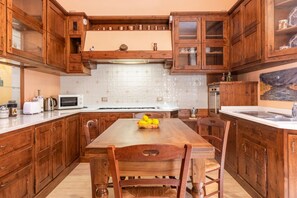 A kitchen with wooden cabinets, a white countertop, a dining table with chairs, and a microwave. - Gemma apartment in Venice (Venezia)