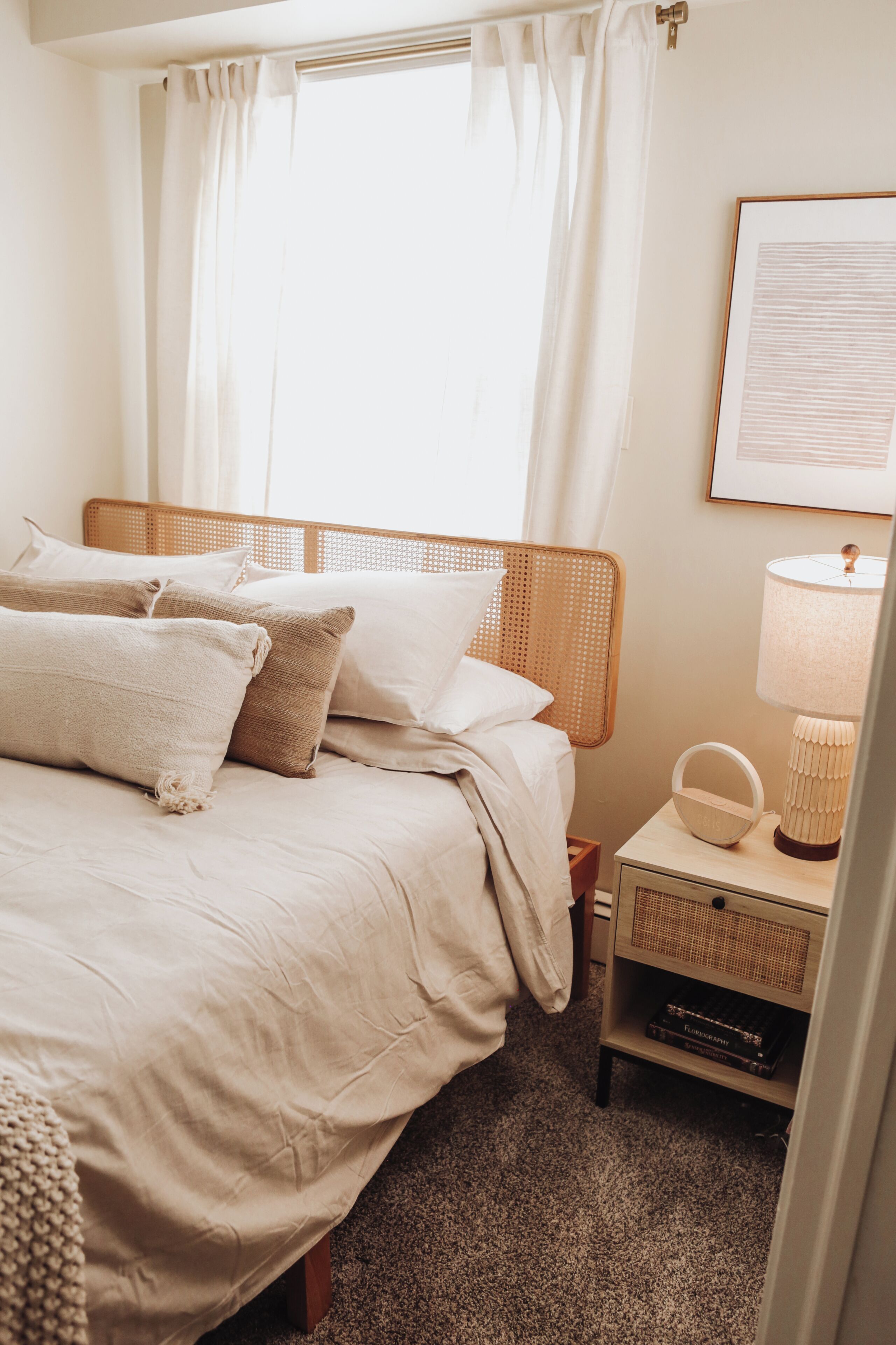 A neatly made bed with a headboard, a bedside table with a lamp, and a framed picture on the wall.